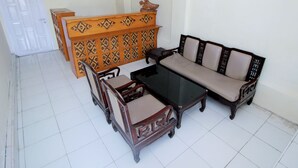 A dining area with a wooden buffet, a glass-top table, and two wooden chairs with cushioned seats. - OYO 1335 Anie 71 Residence (Bengkulu)
