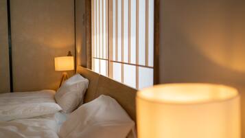Une chambre d’hôtel avec un lit, une table de chevet, une lampe et une fenêtre avec des stores verticaux.