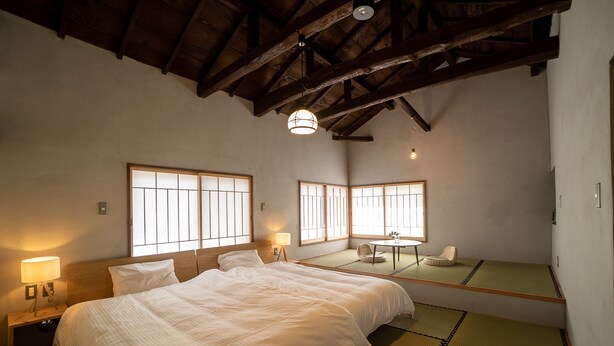 Una habitación japonesa tradicional con suelo de tatami, una cama grande, dos esteras de tatami, una mesita pequeña y una lámpara colgante.