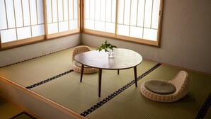 Una habitación con tatami, una mesa redonda, dos cojines y un florero con planta.
