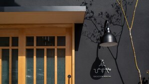 Una puerta de madera con un panel de vidrio, una lámpara de pared y un pequeño árbol.