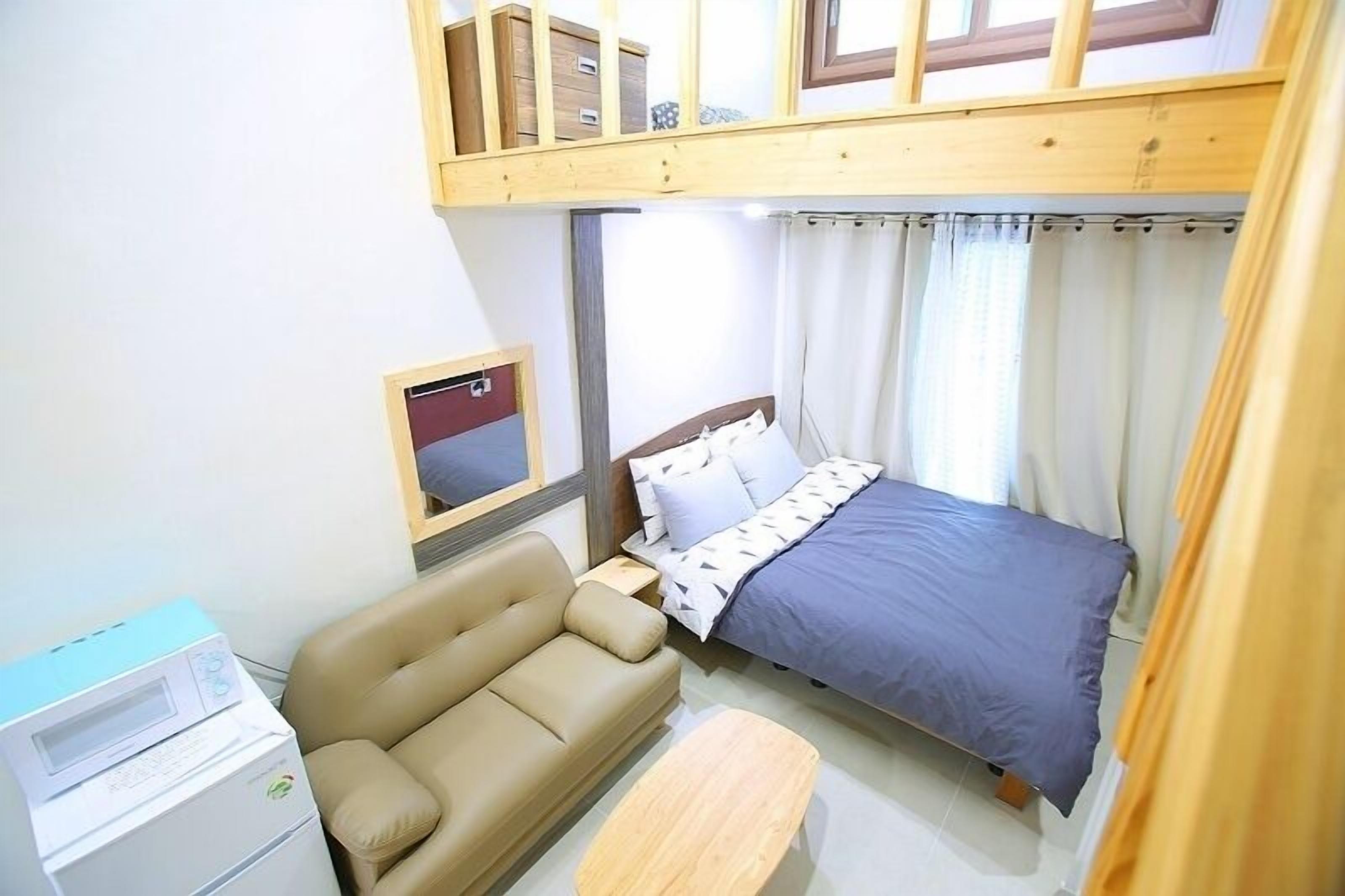 Et soveværelse med køjeseng, sofa, sengebord, lampe og et vindue med gardiner.
