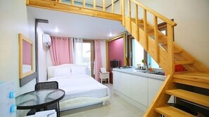Ein Schlafzimmer mit Bett, einem kleinen Tisch, einem Schreibtisch, einer Küchenzeile und einer Holztreppe.