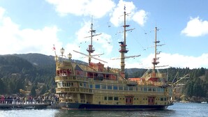 A large, ornate riverboat with multiple decks and a prominent flag, docked at a pier with a forested hillside in the background. - YUPOPPO Hakone (Hakone)