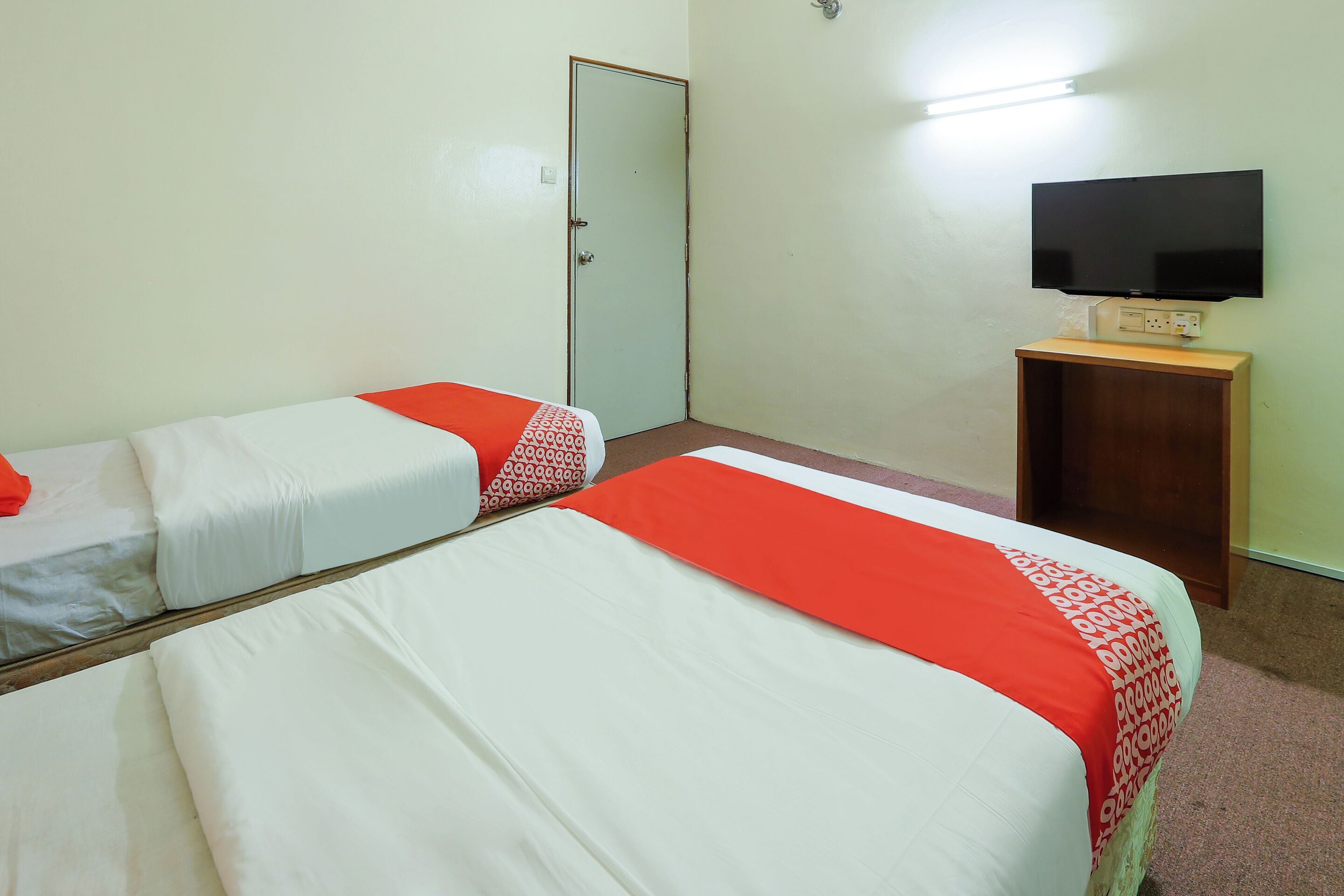 A room with two single beds, each with a red and white bedspread, a television on a wooden stand, and a door.