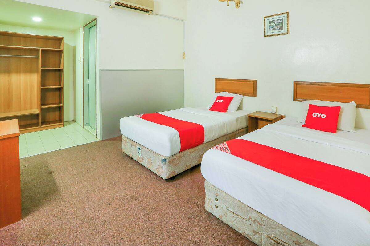 A hotel room with two beds, each with a red OYO branded pillow, a wooden headboard, and a nightstand.