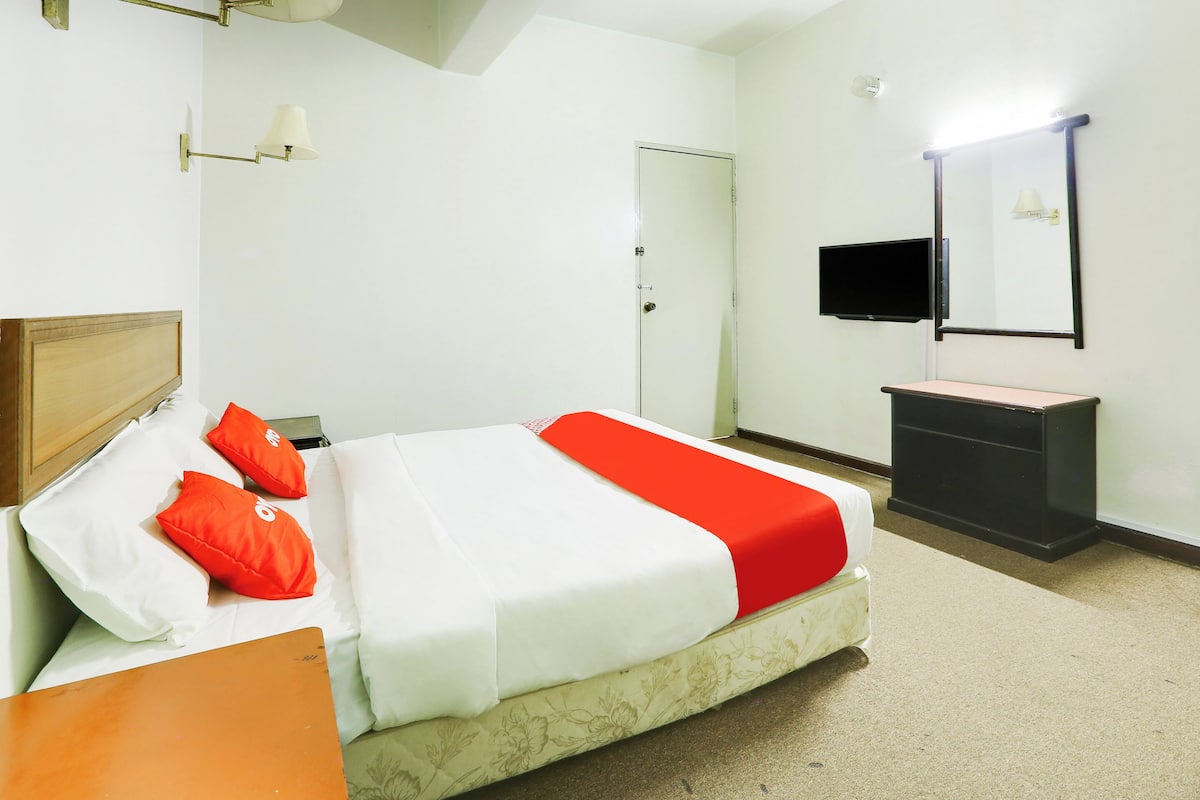 A hotel room with a bed, a nightstand, a dresser, a television, and a door.