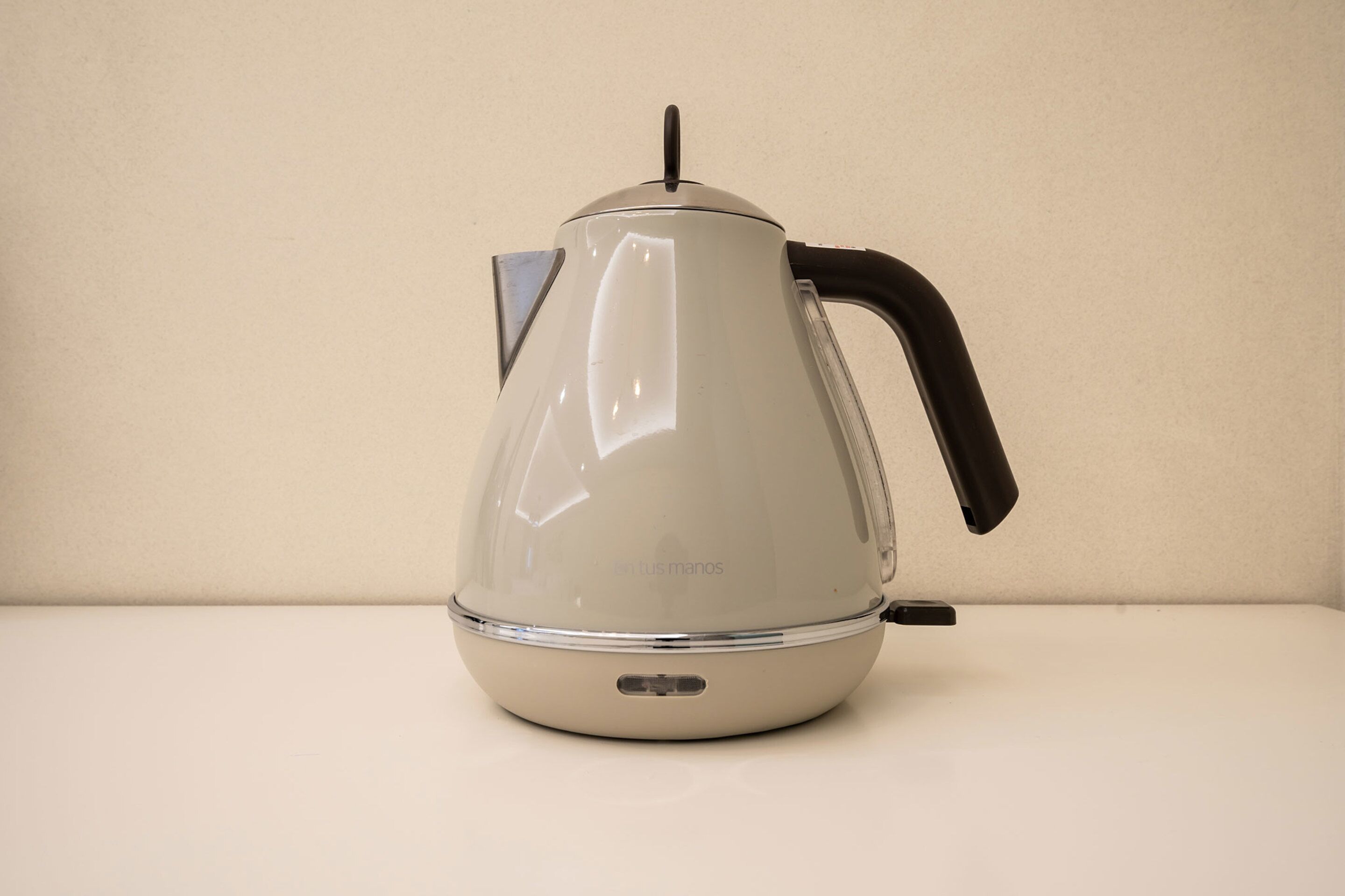 A white electric kettle with a black handle and a transparent lid, placed on a white surface.