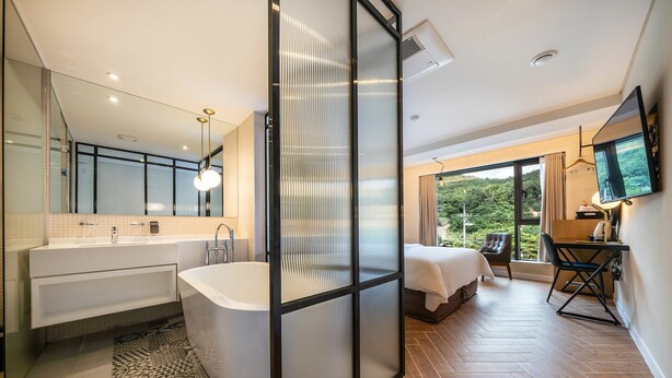 Une chambre d’hôtel moderne dotée d’une grande baignoire, d’une douche séparée, d’un lit avec vue et d’un bureau avec une chaise.