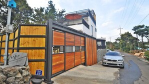 A modern house with a wooden facade, a balcony, and a parked car. - Nonil So Pension (Seogwipo)