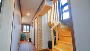 A narrow hallway with wooden flooring, a wooden staircase with a handrail, and a window with blinds. - Nonil So Pension (Seogwipo)