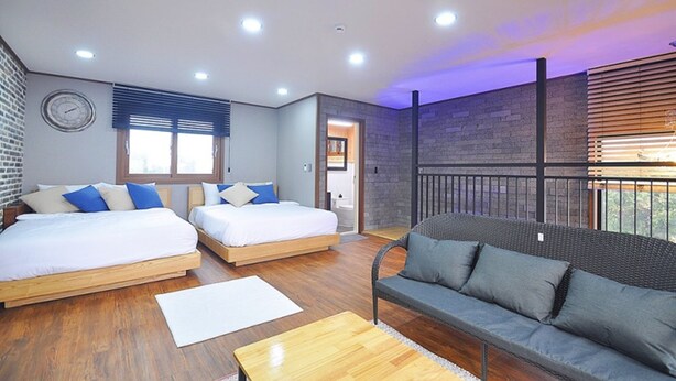 A modern hotel room with two beds, a sofa, wooden flooring, and a balcony with a view. - Nonil So Pension (Seogwipo)