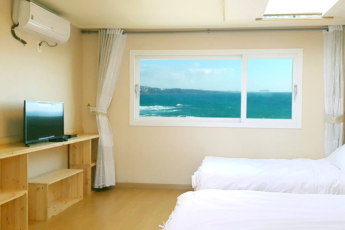 Une chambre avec deux lits, une télévision et une fenêtre donnant sur la mer.