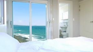 A bedroom with a large sliding glass door leading to a balcony with a view of the sea. - Jeju Witch's Hill (Seogwipo)