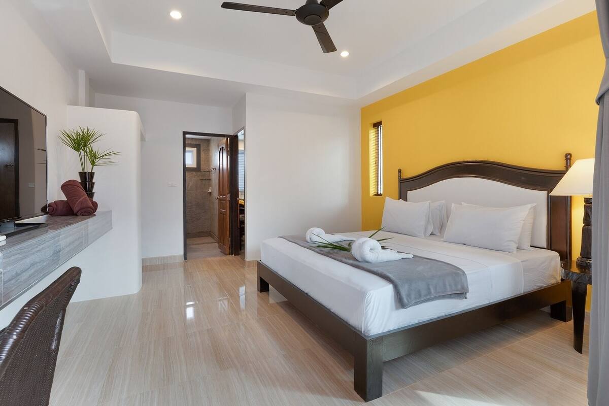 A modern hotel room with a bed, a desk, a television, and a ceiling fan.