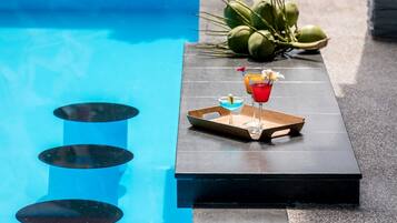 A poolside bar with two drinks on a tray, a pool, and coconuts in the background.