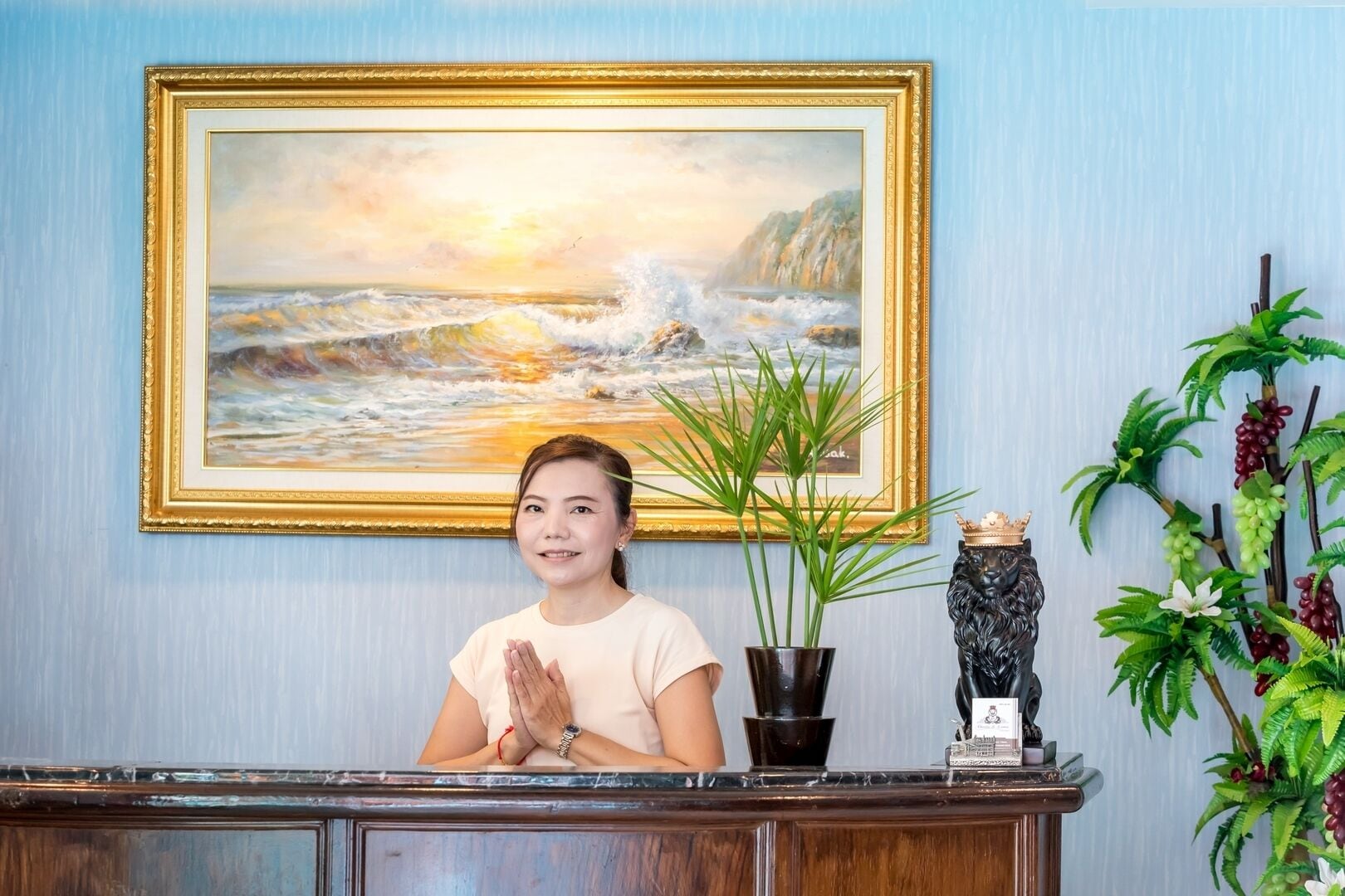 A reception desk with a framed painting of a coastal scene, a potted plant, and a decorative lion head sculpture.