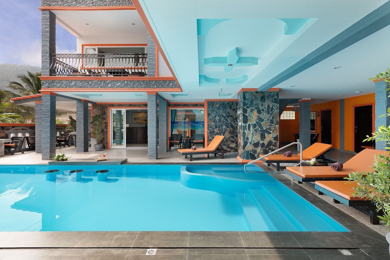 Un hotel moderno con piscina, zonas de descanso y una estructura de dos pisos con detalles de piedra y vidrio.
