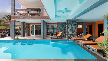 Un hotel moderno con piscina, zonas de descanso y una estructura de dos pisos con detalles de piedra y vidrio.
