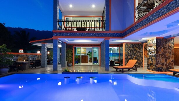 Un edificio de dos pisos con piscina, mobiliario exterior y fachada de piedra.
