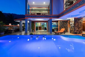 Un edificio de dos pisos con piscina, mobiliario exterior y fachada de piedra.