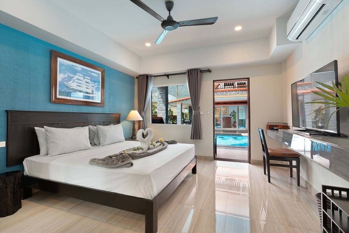 A hotel room with a bed, a TV, a desk, and a view of a pool.