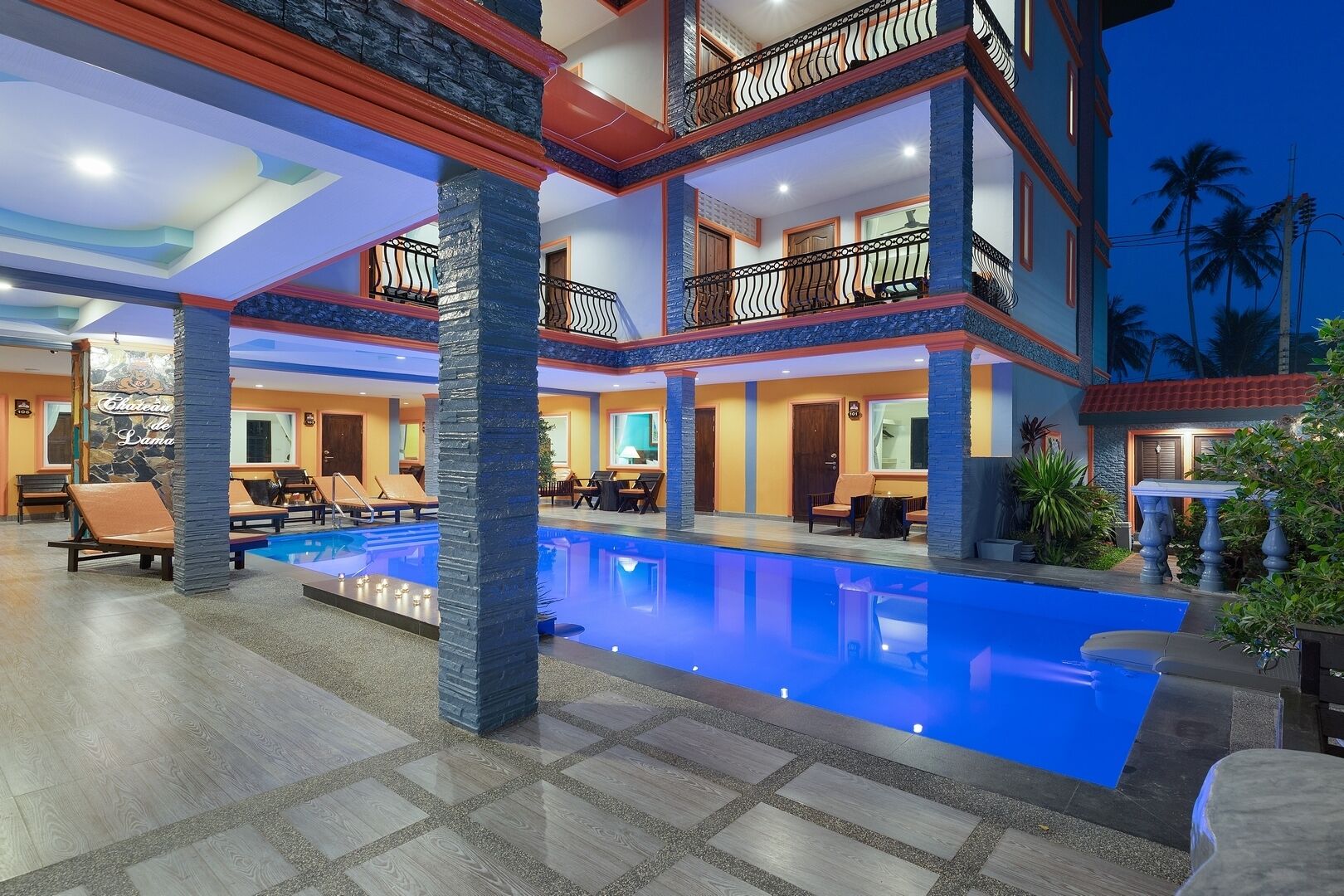 A multi-story hotel with a swimming pool, outdoor seating, and a balcony with a decorative railing.