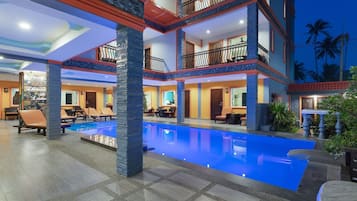 A multi-story hotel with a swimming pool, outdoor seating, and a balcony with a decorative railing.