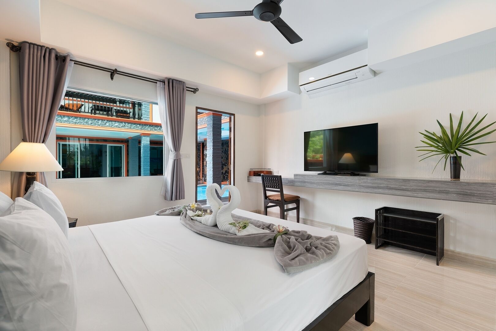 A modern hotel room with a large bed, a flat-screen TV, a ceiling fan, and a view of a building outside.