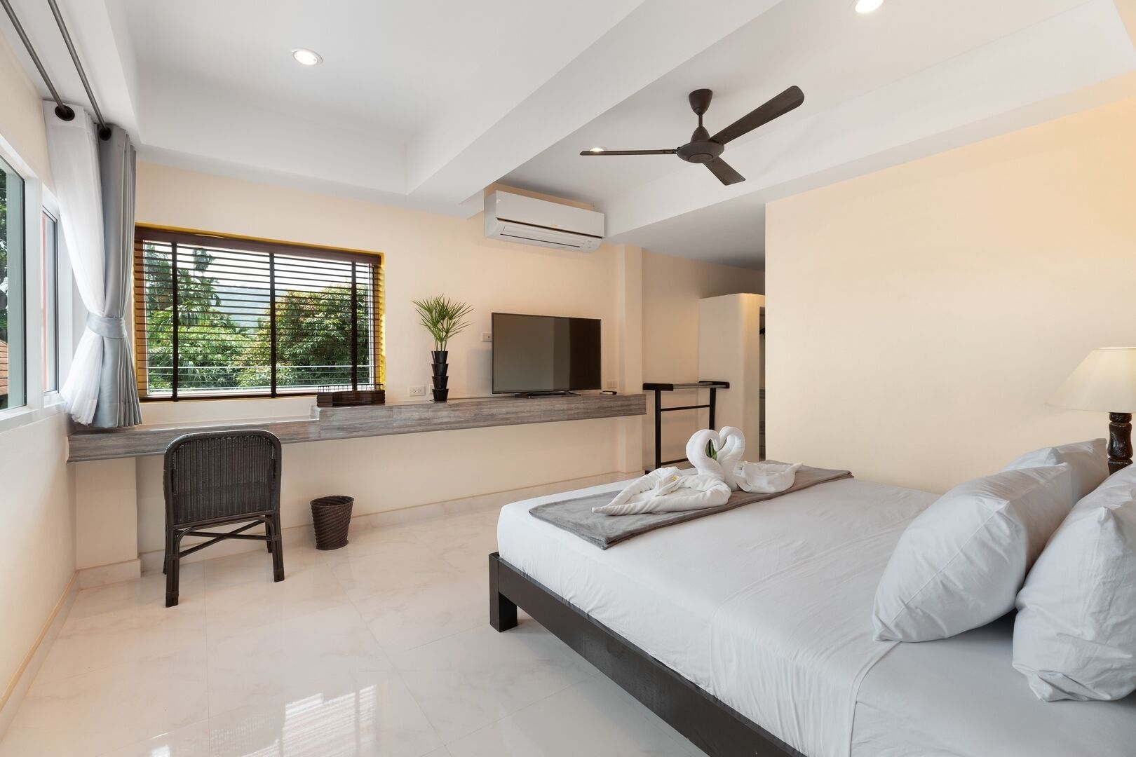A modern hotel room with a bed, a desk, a TV, and a ceiling fan.