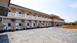 A multi-story hotel with a uniform facade, potted plants along the walkway, and a paved courtyard. - SPOT ON 2027 Putri Guest House Syariah (Cimohong)