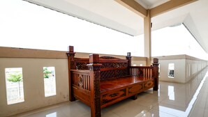 A spacious room with a polished floor, a large bed with intricate woodwork, and a view of a building through a window. - SPOT ON 2027 Putri Guest House Syariah (Cimohong)