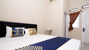A neatly made bed with a blue and yellow patterned bedspread, white pillows, and a black headboard. - SPOT ON 2027 Putri Guest House Syariah (Cimohong)