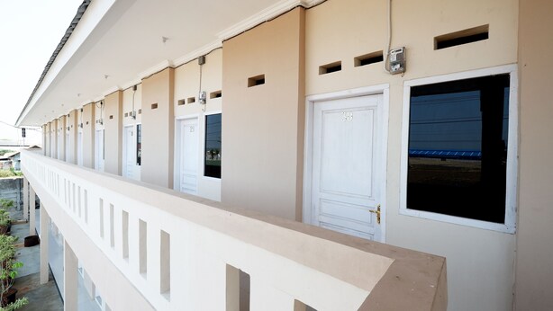 A row of hotel rooms with individual doors and windows, a covered balcony, and a building exterior. - SPOT ON 2027 Putri Guest House Syariah (Cimohong)