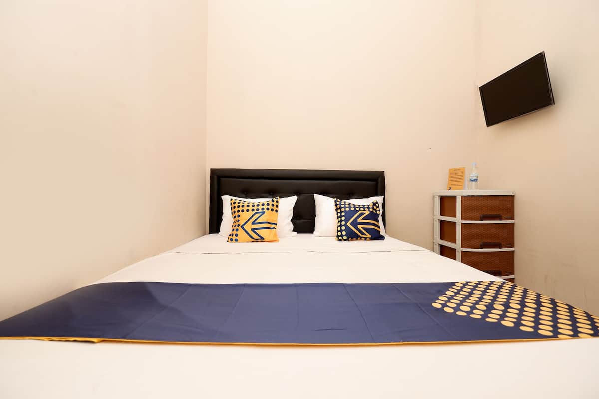 A neatly made bed with a blue and yellow bedspread, two pillows with geometric patterns, and a small wooden side table with a water bottle.