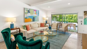A modern living room with a sofa, two green velvet chairs, a glass coffee table, and a painting on the wall. - Belding Bliss (Palm Springs)