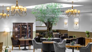 A dining area with round tables, grey upholstered chairs, and a central tree. - Ventus Rosa Boutique Aparthotel (Kraków)
