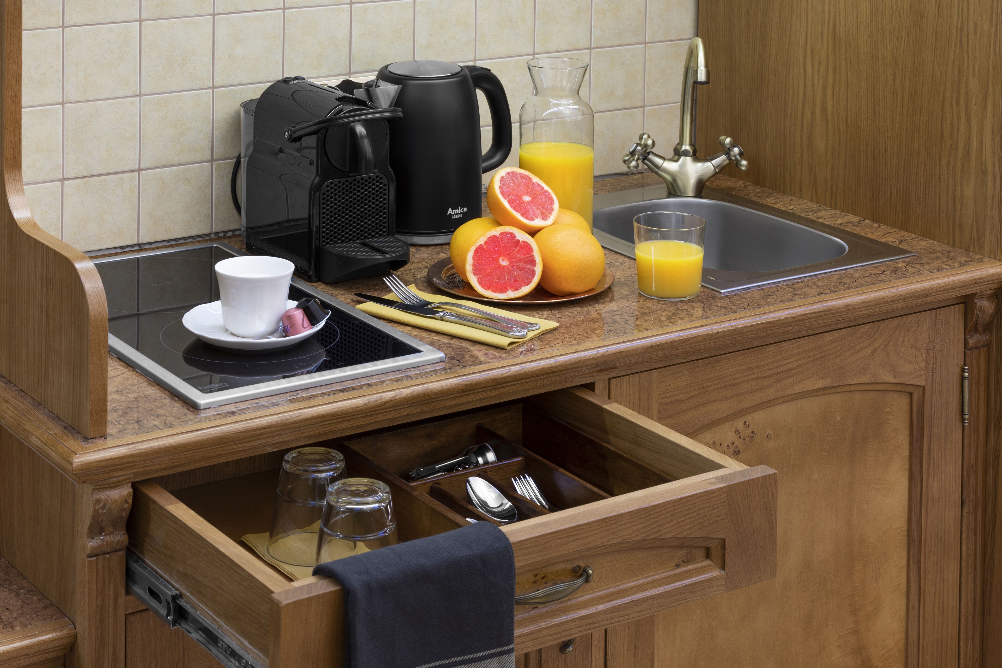 A kitchen with a coffee maker, a sink, and a breakfast setup including grapefruit and orange juice.