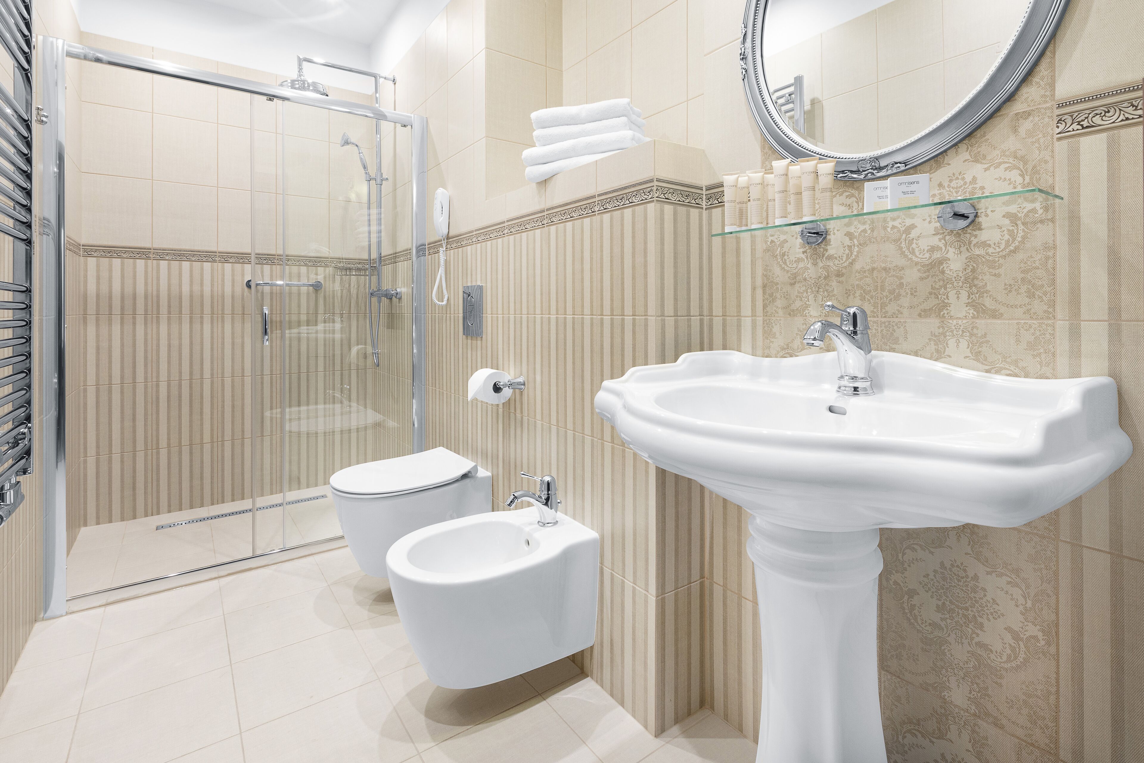 A modern bathroom with a glass shower enclosure, a pedestal sink, and a bidet.