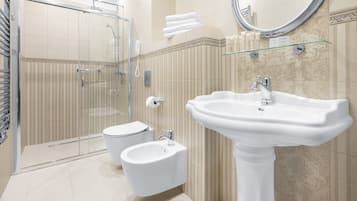 A modern bathroom with a glass shower enclosure, a pedestal sink, and a bidet.