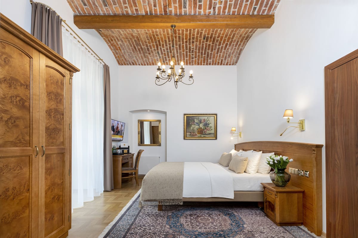 Une chambre à coucher avec un grand lit, une armoire en bois, un bureau et un lustre.