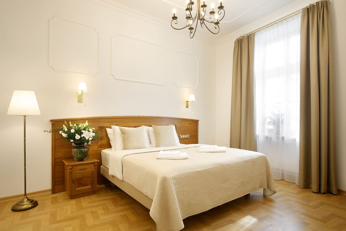 Un lit bien fait, avec une tête de lit, une lampe de chevet et un vase de fleurs posé sur une table de chevet.