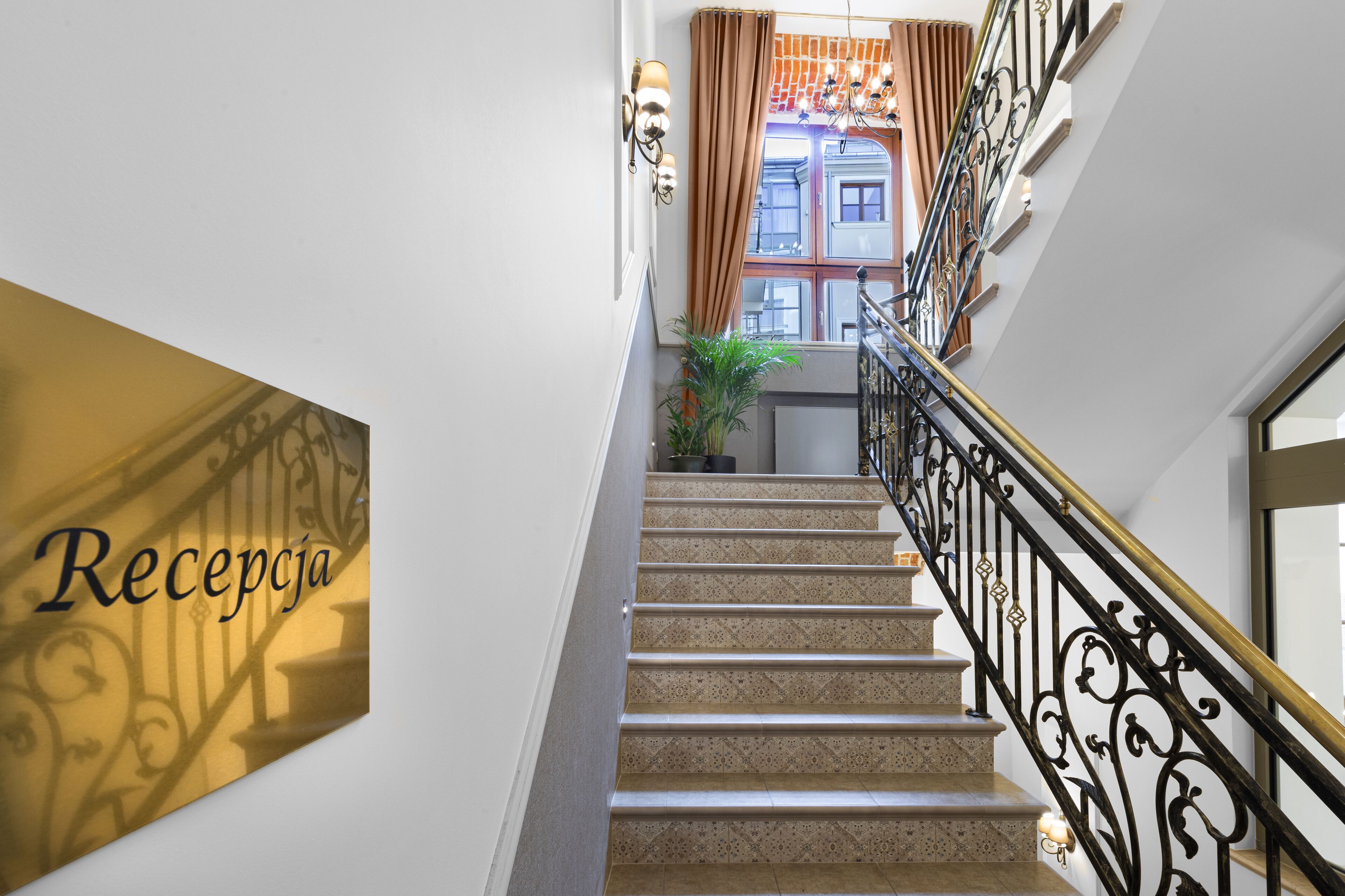 A staircase with a sign reading "Recepcja" on the left, leading to a room with a window and a plant.