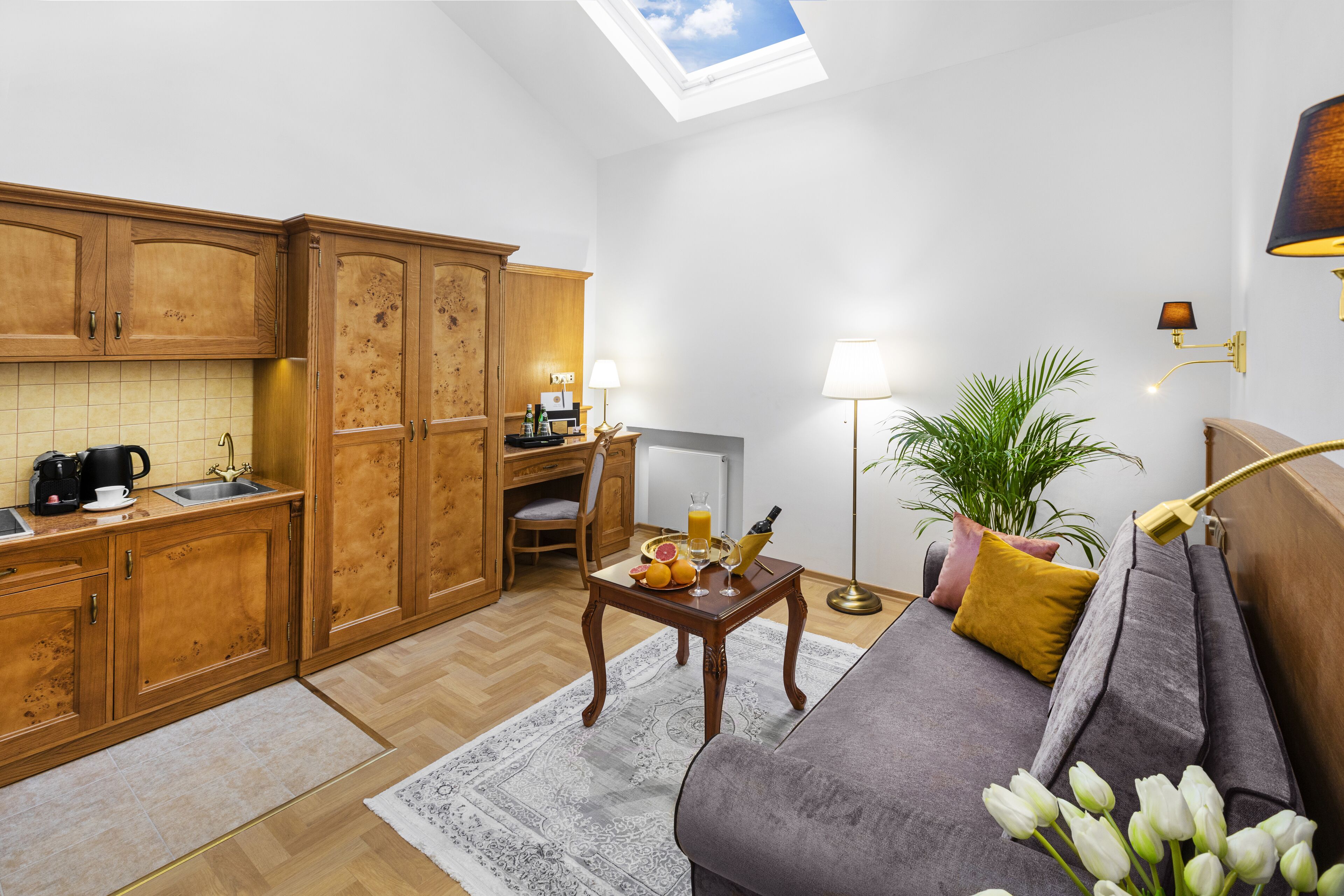 A compact living space with a kitchenette, a sofa, a dining table with fruits and a bottle, and a skylight.