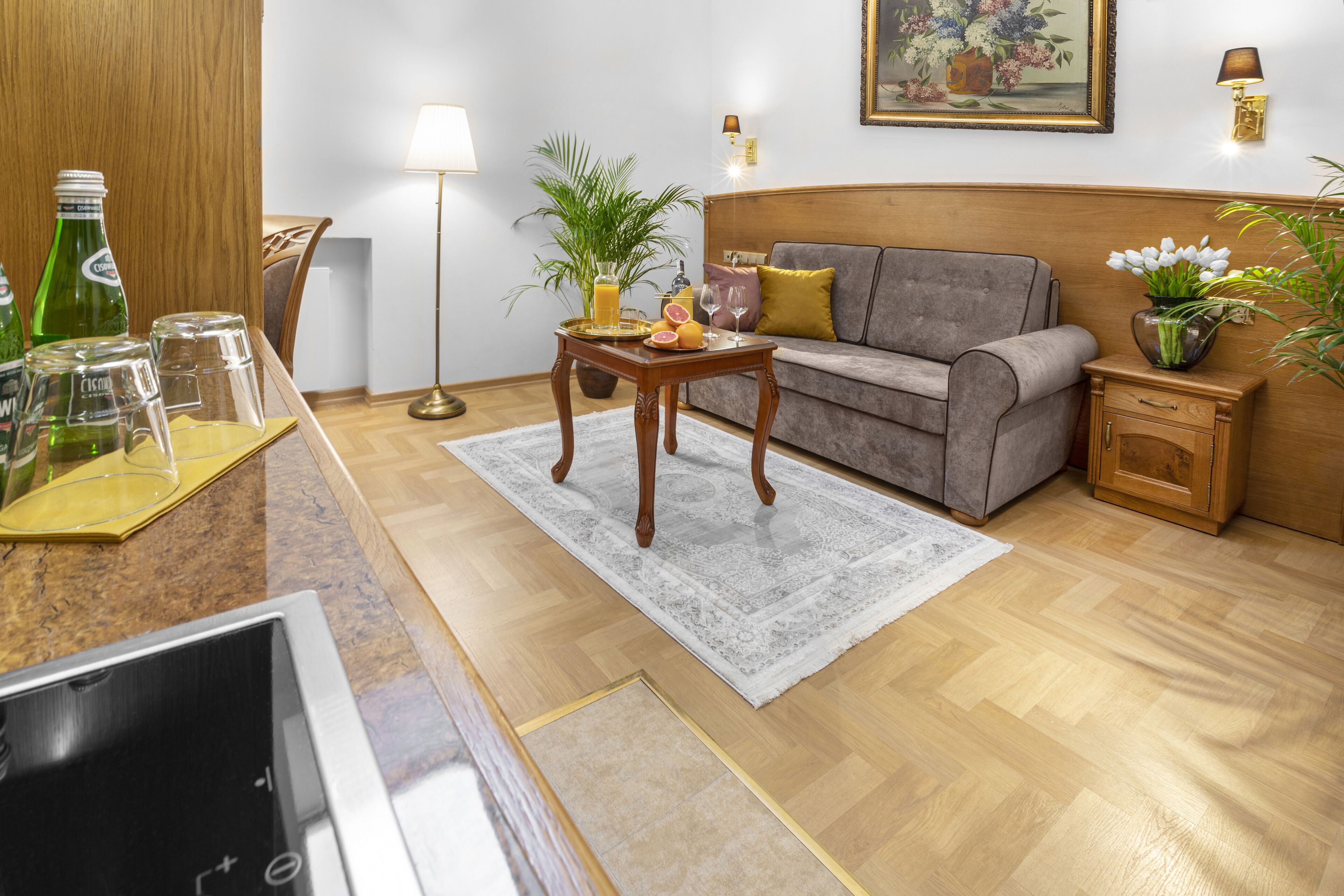 A living room with a sofa, a small table with drinks, a lamp, and a painting on the wall.