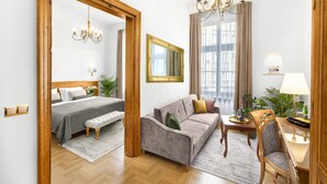 A hotel room with a bed, a sofa, a dining table, and a chandelier. - Ventus Rosa Boutique Aparthotel (Kraków)