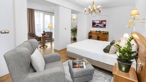 A hotel room with a large bed, a grey armchair, a small ottoman, a wooden side table with a plant, and a television mounted on the wall. - Ventus Rosa Boutique Aparthotel (Kraków)