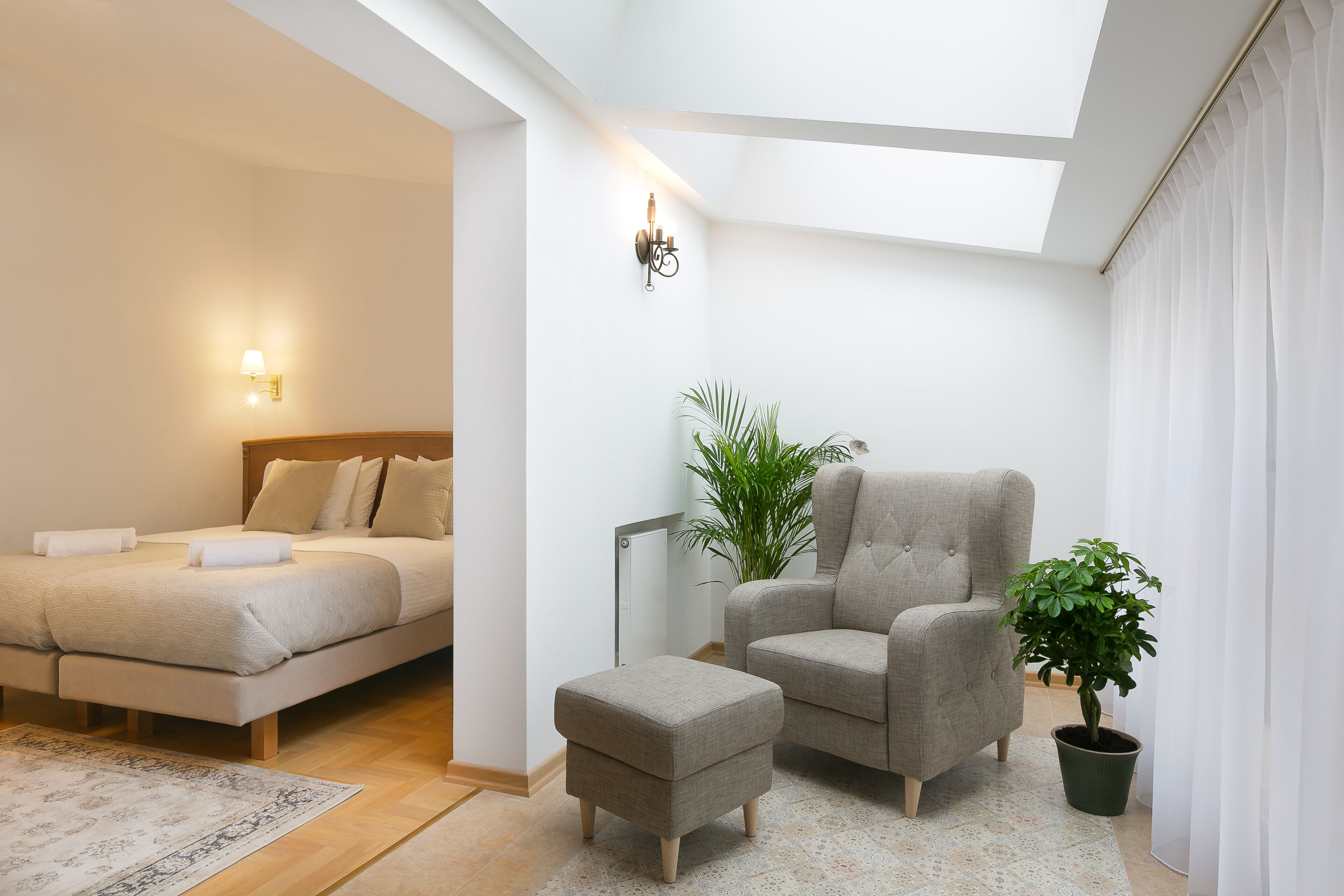Une chambre à coucher comprenant un lit, une chaise, une petite table, une plante en pot et une lucarne.