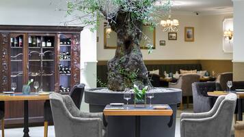 A restaurant with a central tree planter, dining tables, chairs, and a wine display cabinet.