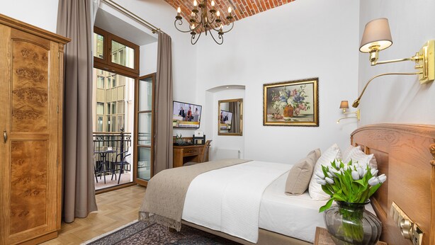 A bedroom with a bed, a nightstand, a vase with flowers, a television, and a view of the outside. - Ventus Rosa Boutique Aparthotel (Kraków)